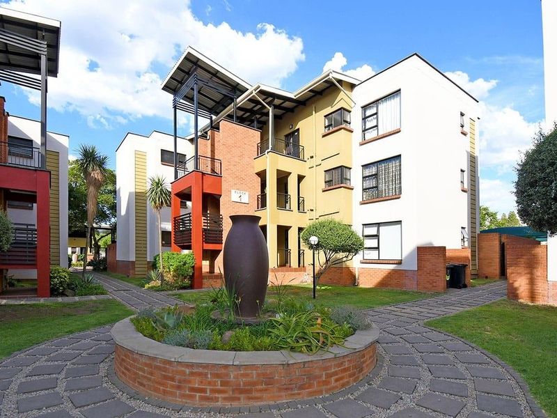 A well-maintained apartment complex exterior featuring brick paved walkways, a central brick planter, and multi-story residential blocks with private balconies.
