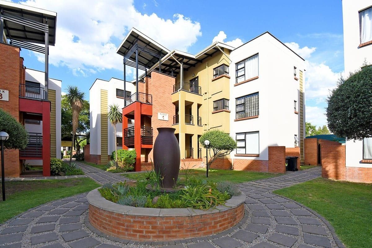 A well-maintained apartment complex exterior featuring brick paved walkways, a central brick planter, and multi-story residential blocks with private balconies.