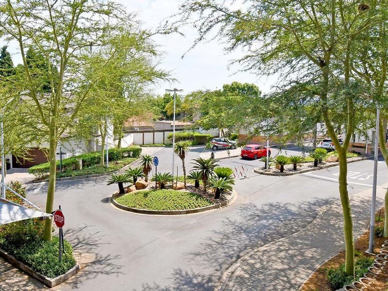 An elevated view of the complex entrance featuring a landscaped roundabout, paved driveway, and established trees within a secure residential estate.