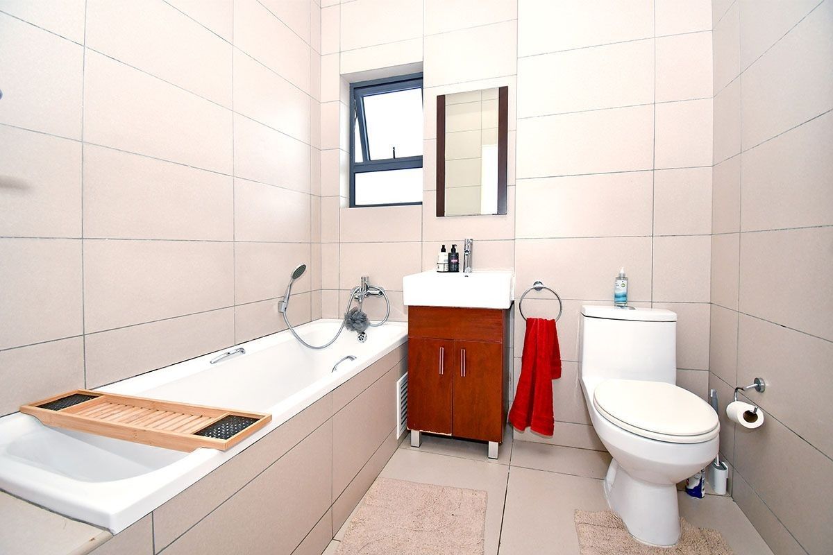 A well-maintained bathroom featuring full-height wall tiling, a built-in bathtub, a vanity basin, and a standard toilet.