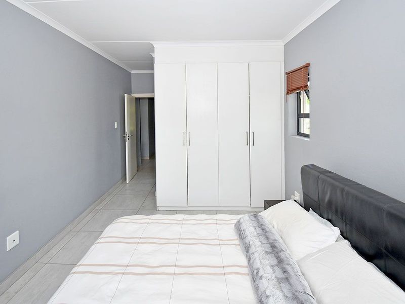 A well-maintained bedroom featuring neutral grey walls, tiled flooring, and ample built-in cupboard storage.