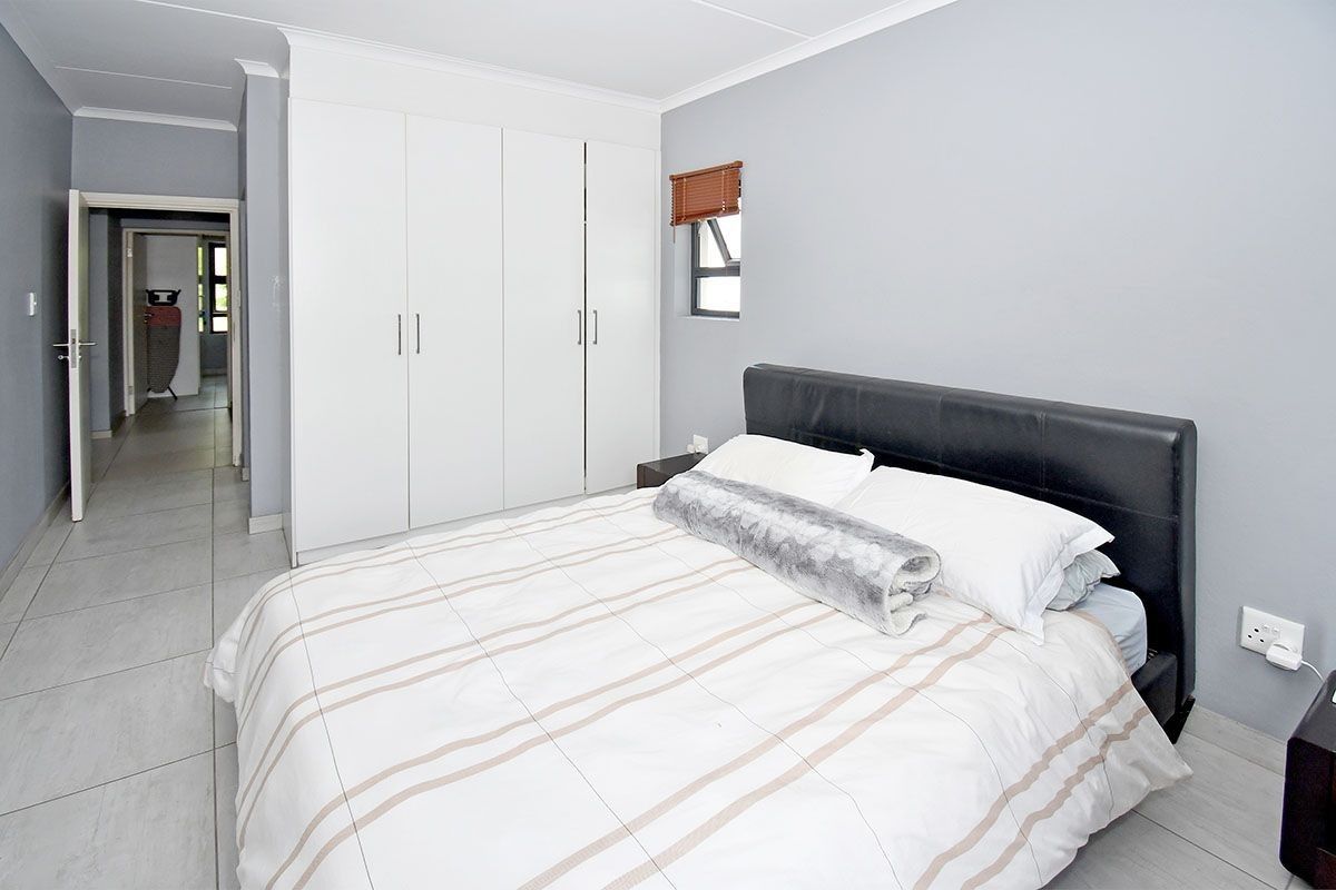 A well-maintained bedroom featuring neutral grey walls, tiled flooring, and ample built-in cupboard storage.