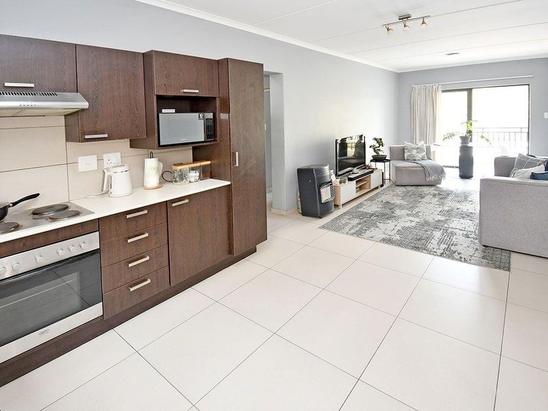 Open-plan living area featuring a modern kitchen with dark wood cabinetry, integrated appliances, and tiled flooring, leading to a bright balcony.