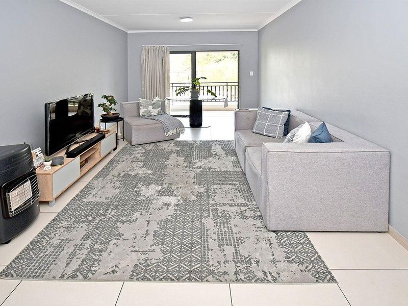 A bright and neutral living room featuring large format floor tiles, clean wall finishes, and a sliding glass door leading to an outdoor balcony area.