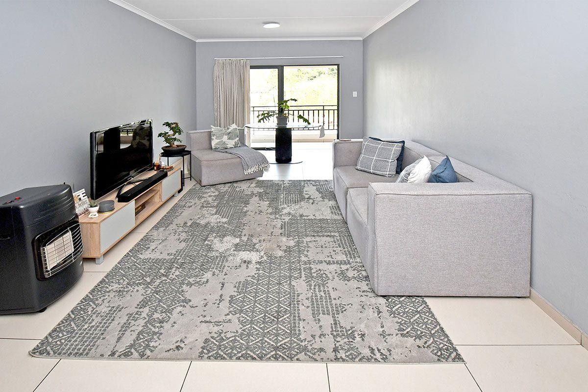 A bright and neutral living room featuring large format floor tiles, clean wall finishes, and a sliding glass door leading to an outdoor balcony area.
