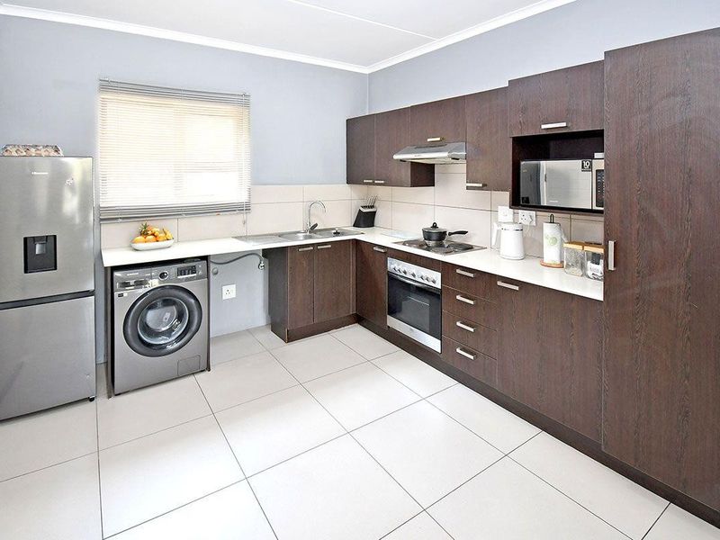 Modern kitchen featuring dark wood cabinetry, light countertops, integrated appliances, and tiled flooring, offering a clean and functional workspace.