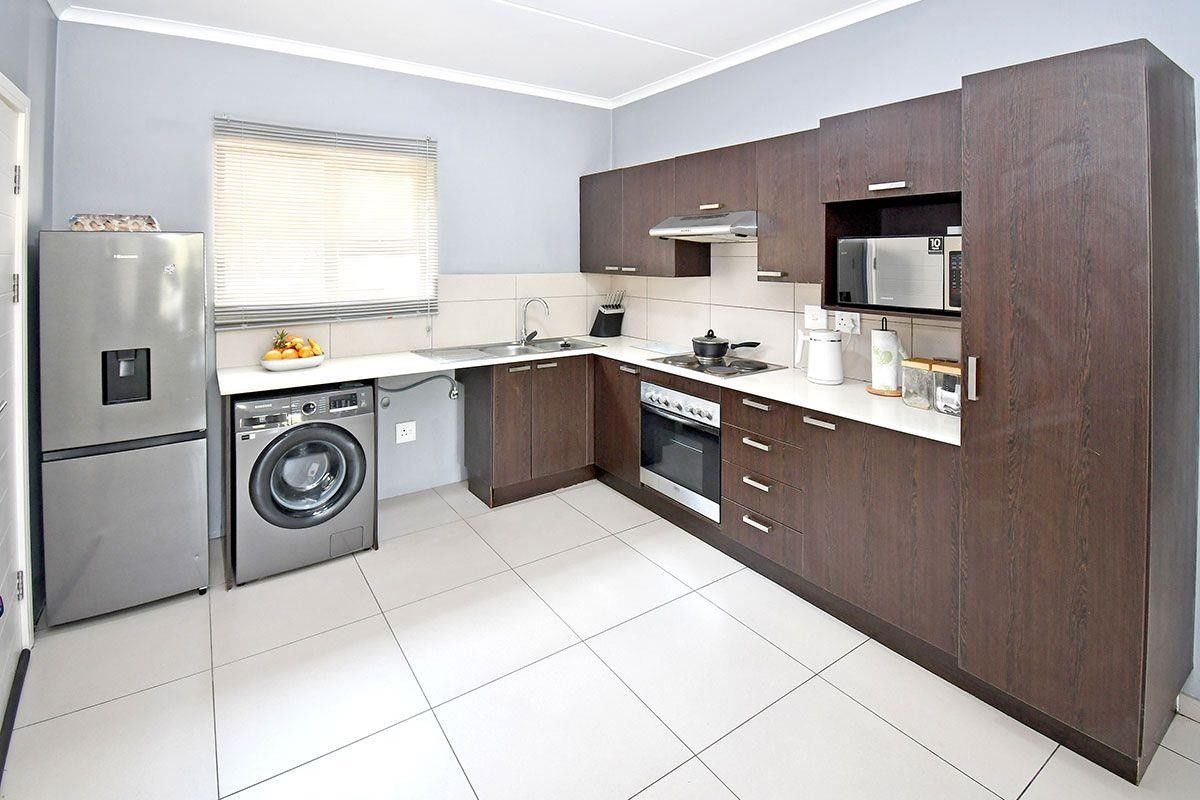 Modern kitchen featuring dark wood cabinetry, light countertops, integrated appliances, and tiled flooring, offering a clean and functional workspace.