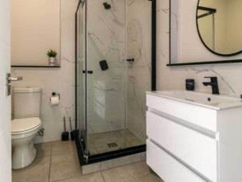 Modern bathroom featuring a glass shower enclosure, sleek white vanity with black tapware, and contemporary marble-look wall tiling.