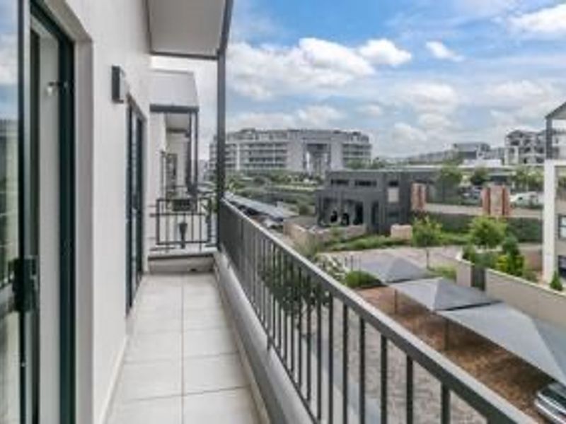 A clean, modern balcony featuring tiled flooring and a metal balustrade, offering an elevated view of the surrounding apartment complex and parking area.