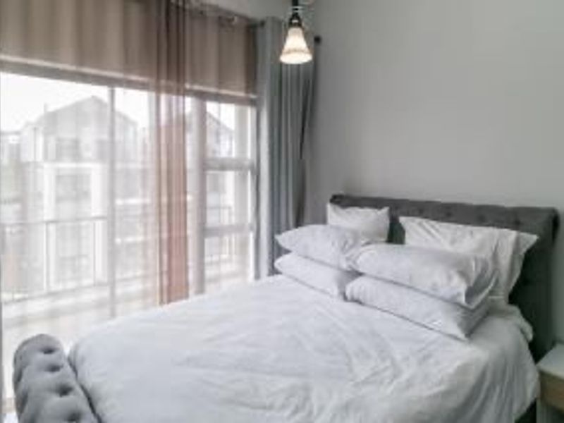 A well-lit bedroom featuring a large sliding glass door with curtains, providing natural light and access to an outdoor balcony area.