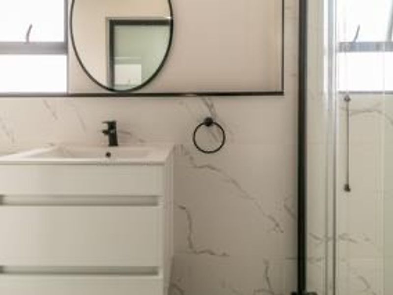 Modern bathroom featuring a sleek white vanity, black tapware, marble-look wall tiles, and a glass shower enclosure.