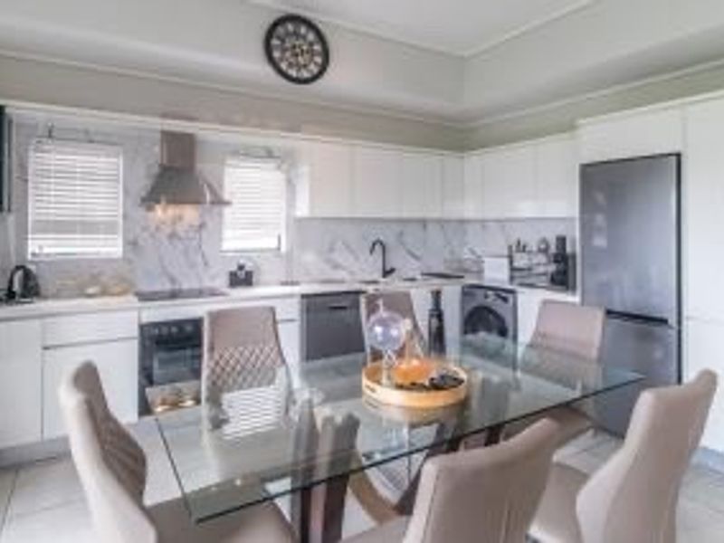 Modern open-plan kitchen and dining area featuring sleek white cabinetry, marble-look splashbacks, integrated appliances, and contemporary tiled flooring.