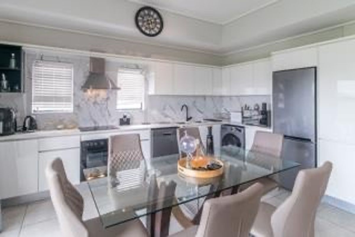 Modern open-plan kitchen and dining area featuring sleek white cabinetry, marble-look splashbacks, integrated appliances, and contemporary tiled flooring.