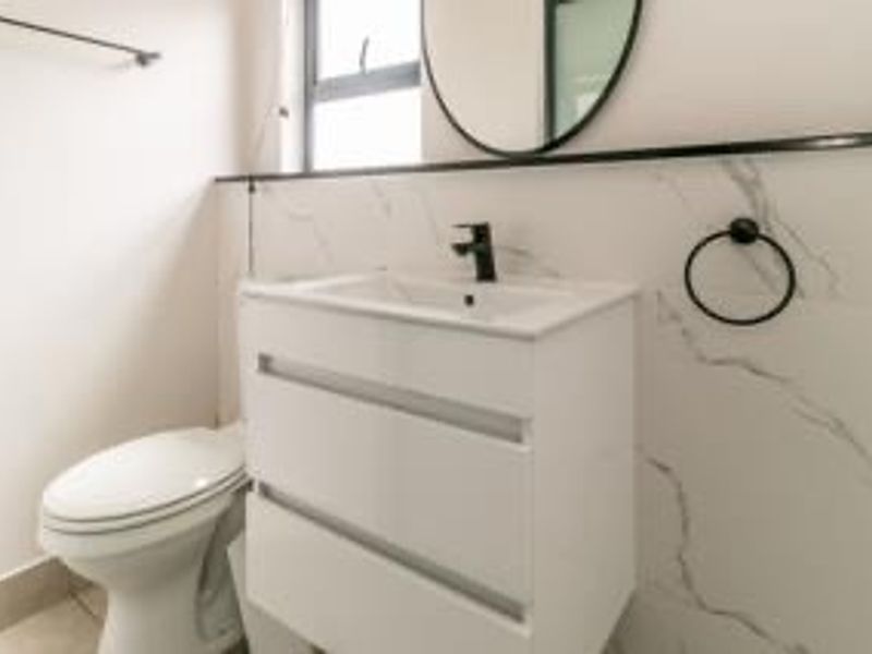 Modern bathroom featuring a sleek white vanity with a black mixer tap, marble-look wall tiling, and contemporary fixtures.