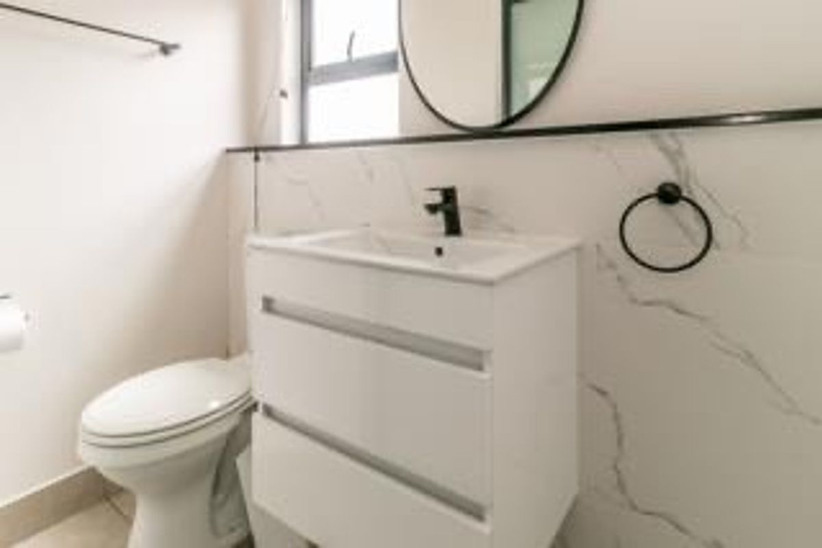 Modern bathroom featuring a sleek white vanity with a black mixer tap, marble-look wall tiling, and contemporary fixtures.