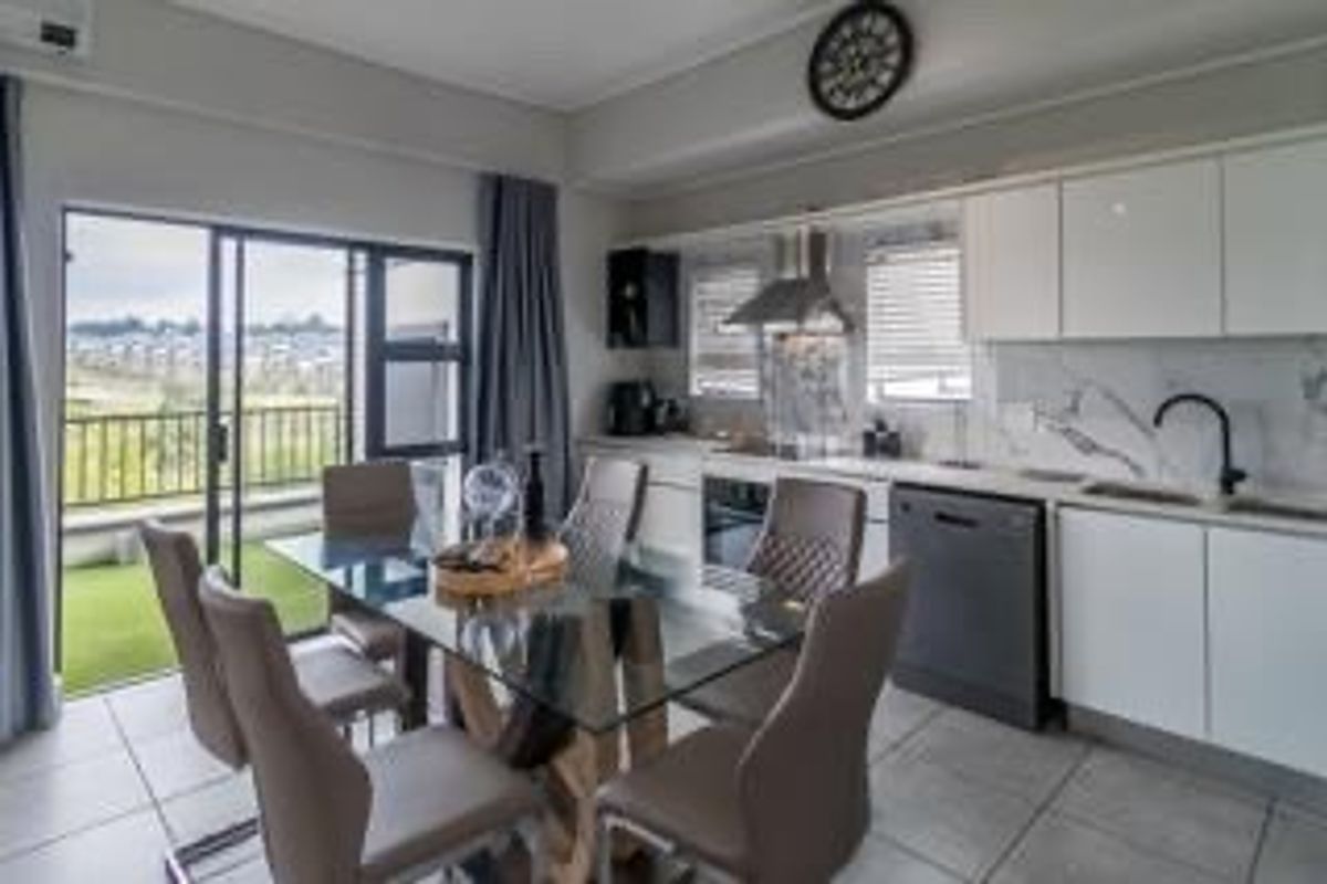 Modern open-plan kitchen and dining area featuring sleek white cabinetry, integrated appliances, marble-look backsplash, and direct access to a balcony through sliding glass doors.