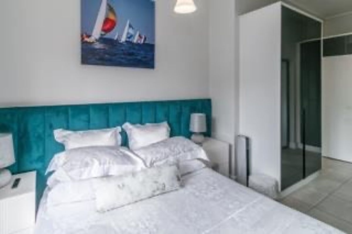 A well-maintained bedroom featuring a modern built-in wardrobe with mirrored doors and neutral tiled flooring.