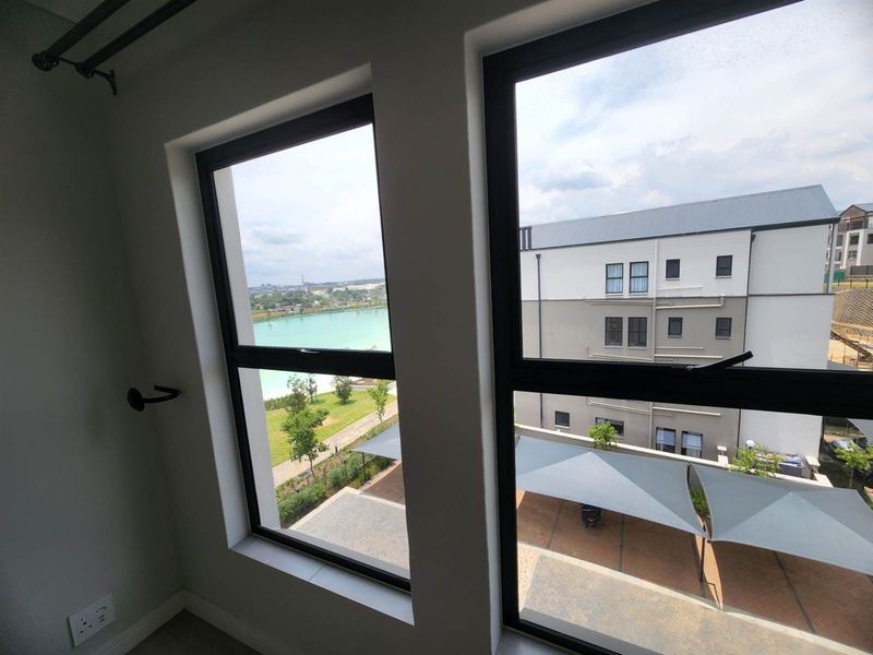 A view from an apartment window overlooking a landscaped area, a lake, and neighbouring residential buildings.