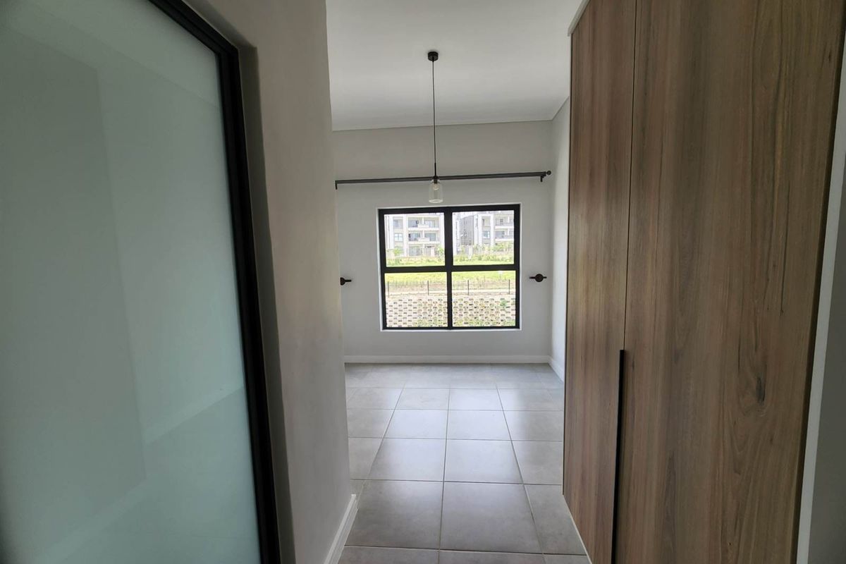 A bright, empty bedroom featuring modern tiled flooring, built-in wooden cupboards, and a large window providing natural light.