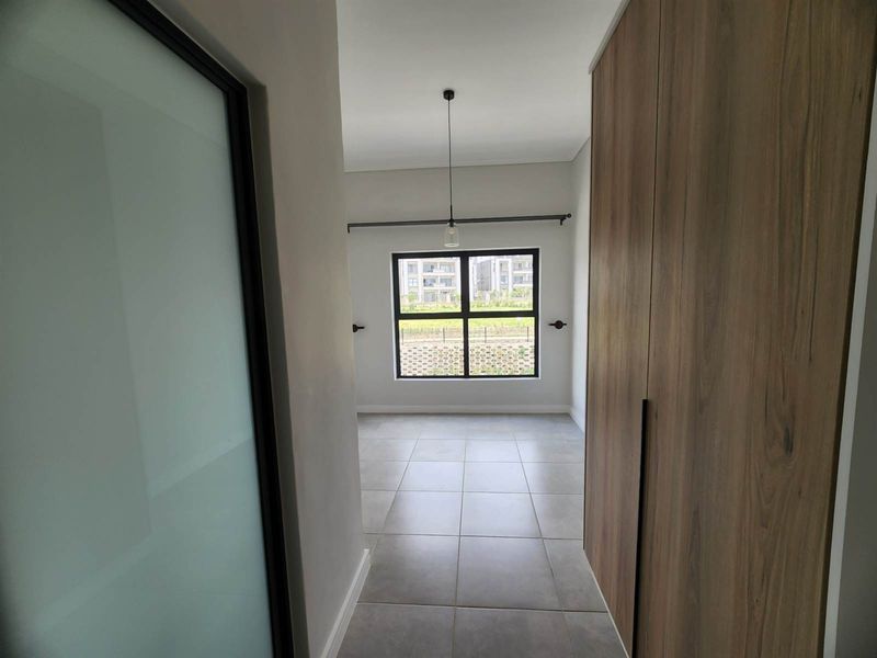 A bright, empty bedroom featuring modern tiled flooring, built-in wooden cupboards, and a large window providing natural light.