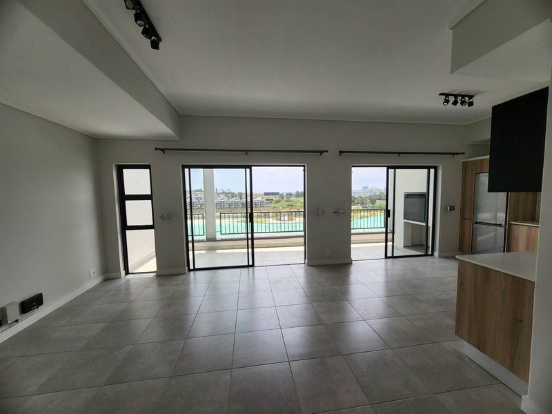 Spacious open-plan living area featuring modern tiled floors, track lighting, and seamless access to a balcony with a built-in braai.