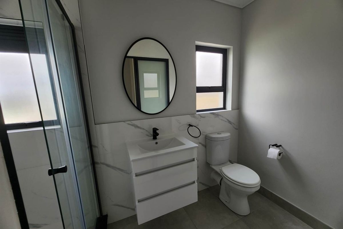 Modern bathroom featuring a floating vanity, black tapware, marble-look wall tiling, and a glass-enclosed shower.