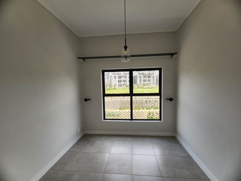 A clean, empty bedroom featuring neutral tiled flooring, a modern pendant light, and a large window with an installed curtain rod.
