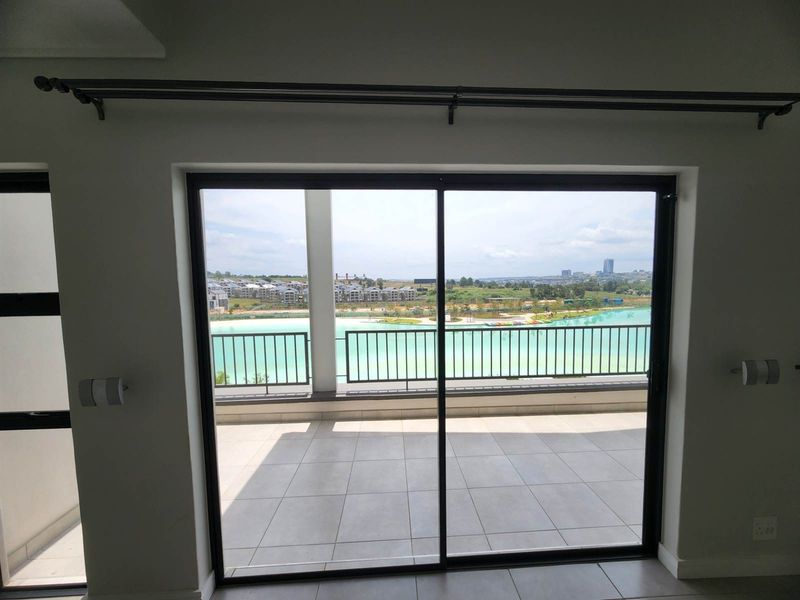 A view from an interior space looking out through a sliding glass door onto a tiled balcony with a scenic lagoon and estate view.
