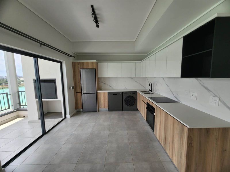 Modern kitchen featuring sleek white and wood-grain cabinetry, stone countertops, marble-look splashback, and integrated appliances, with direct access to a balcony.