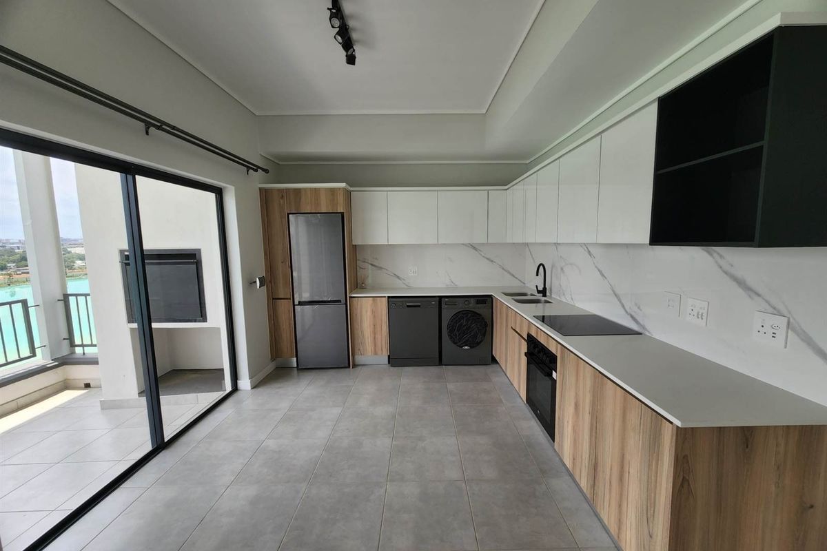 Modern kitchen featuring sleek white and wood-grain cabinetry, stone countertops, marble-look splashback, and integrated appliances, with direct access to a balcony.