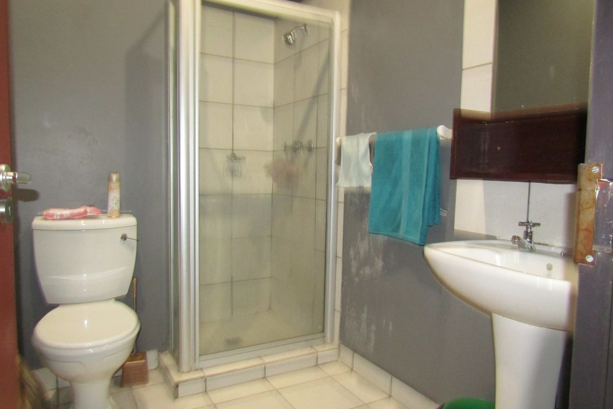 A compact bathroom featuring a shower enclosure, pedestal basin, and toilet, currently showing signs of wear and wall surface damage.