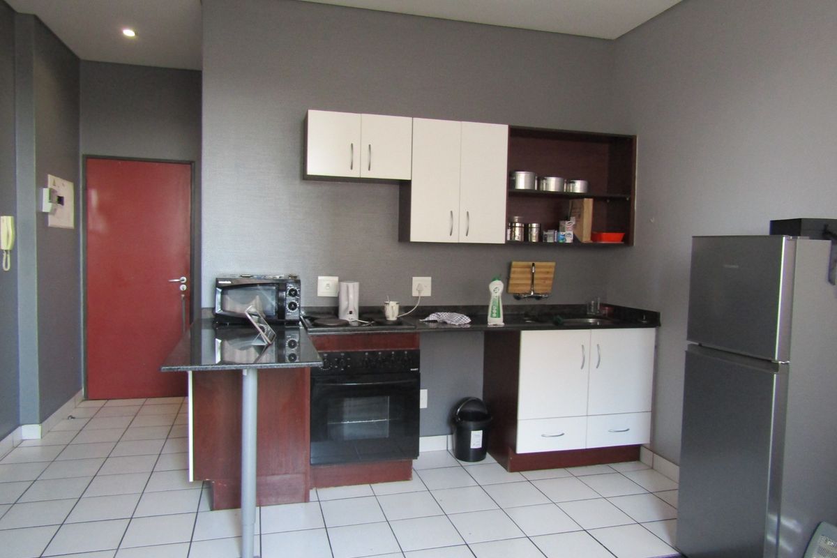 Compact kitchen featuring two-tone cabinetry, granite countertops, built-in oven and hob, and tiled flooring in an open-plan layout.