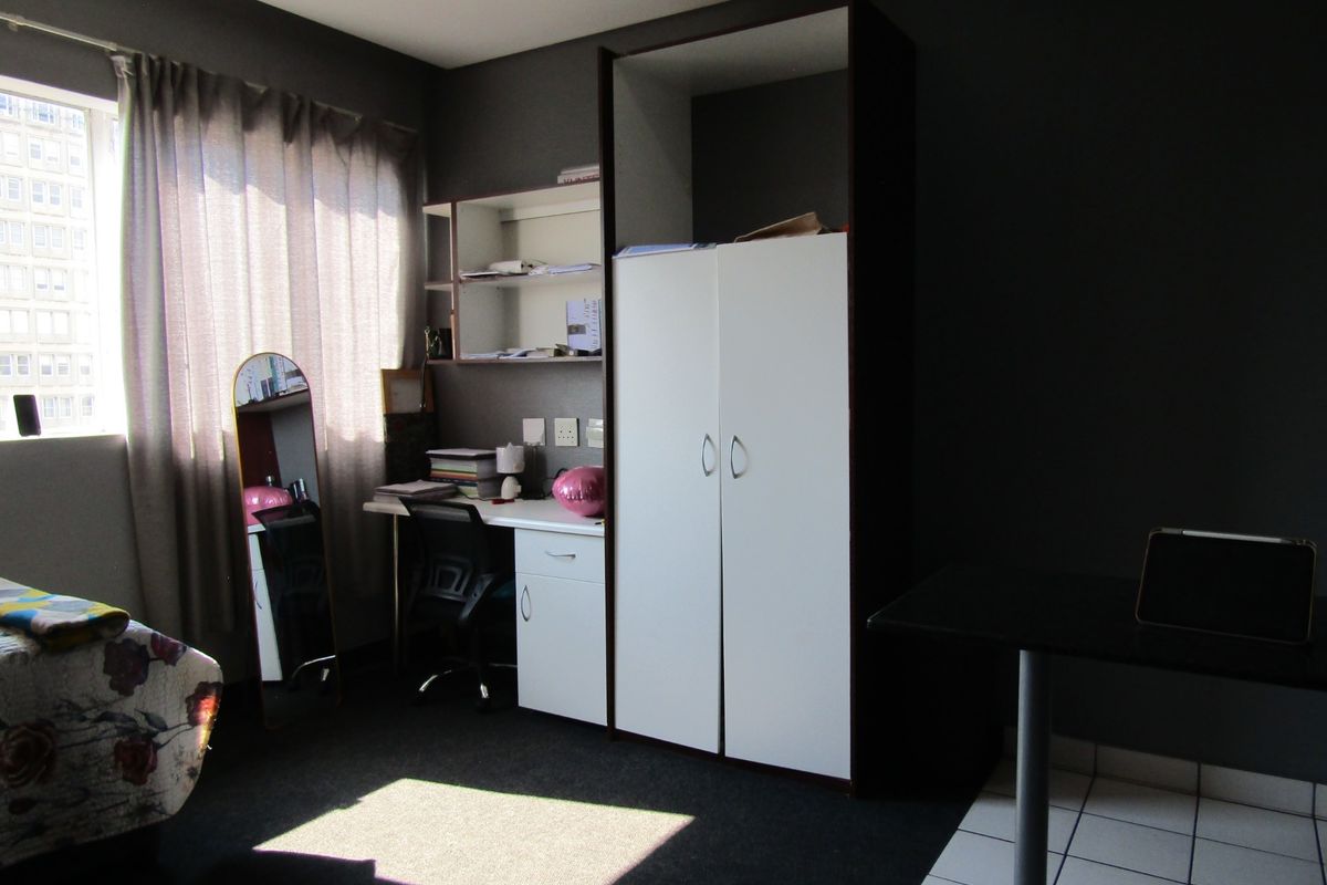 A bedroom featuring built-in cabinetry, including a desk, shelving, and a wardrobe, with dark wall finishes and carpeted flooring.