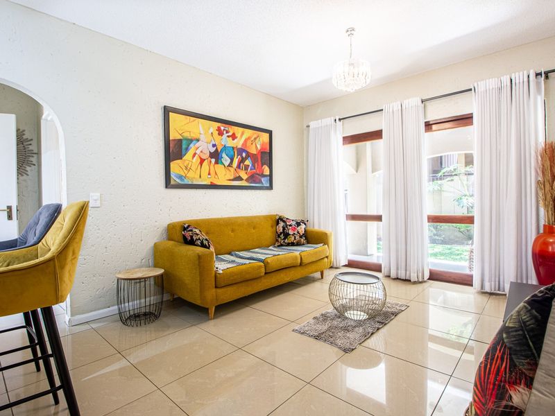 A bright living room featuring polished tile flooring, an elegant crystal chandelier, and large sliding glass doors that provide access to the outdoor area.
