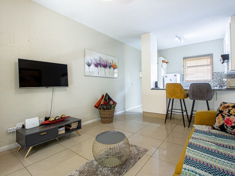 Open-plan living area featuring tiled flooring, a textured wall finish, and a functional kitchen with built-in cabinetry and a breakfast counter.