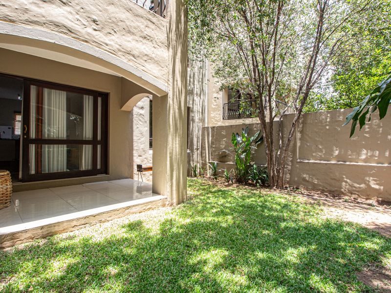 A private rear garden featuring a covered patio with tiled flooring, accessible via sliding glass doors, complemented by a well-maintained lawn and boundary wall.