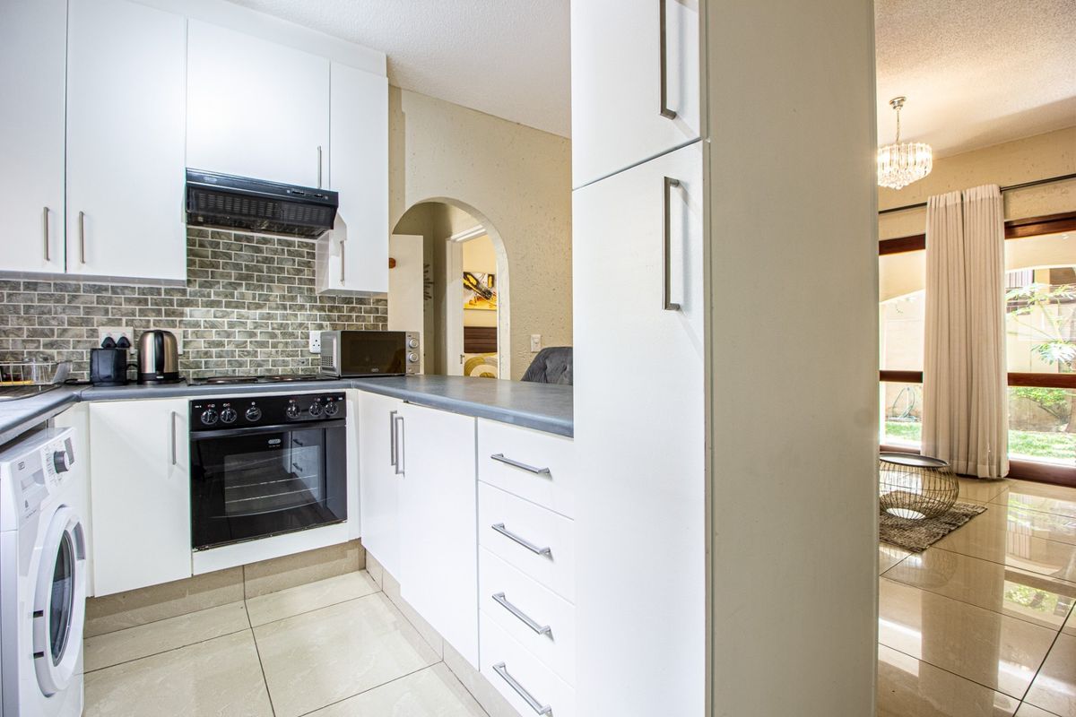 A modern kitchen featuring white cabinetry, dark countertops, a tiled backsplash, and integrated appliances, flowing into an adjacent living area.