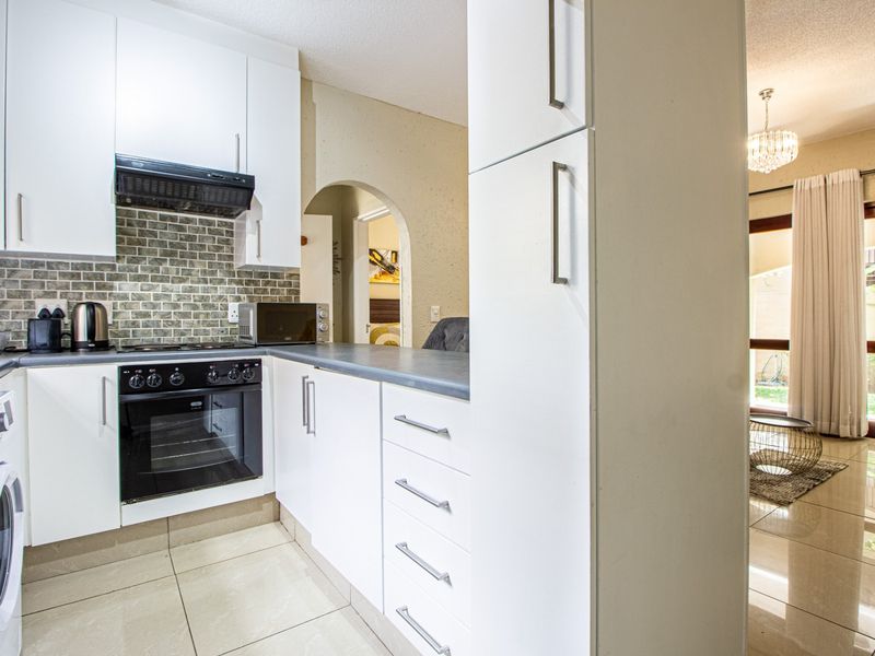 A modern kitchen featuring white cabinetry, dark countertops, a tiled backsplash, and integrated appliances, flowing into an adjacent living area.