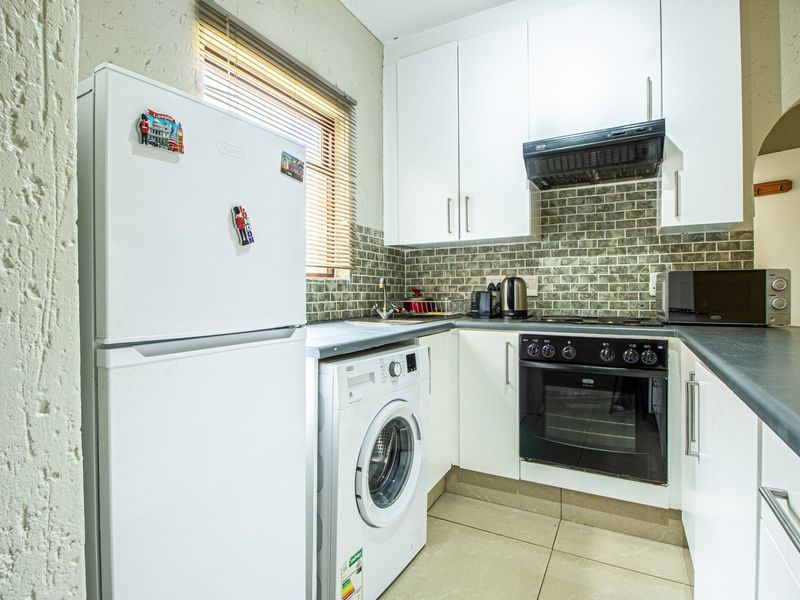 Compact kitchen featuring white cabinetry, subway tile backsplash, built-in oven with hob, extractor fan, and tiled flooring.