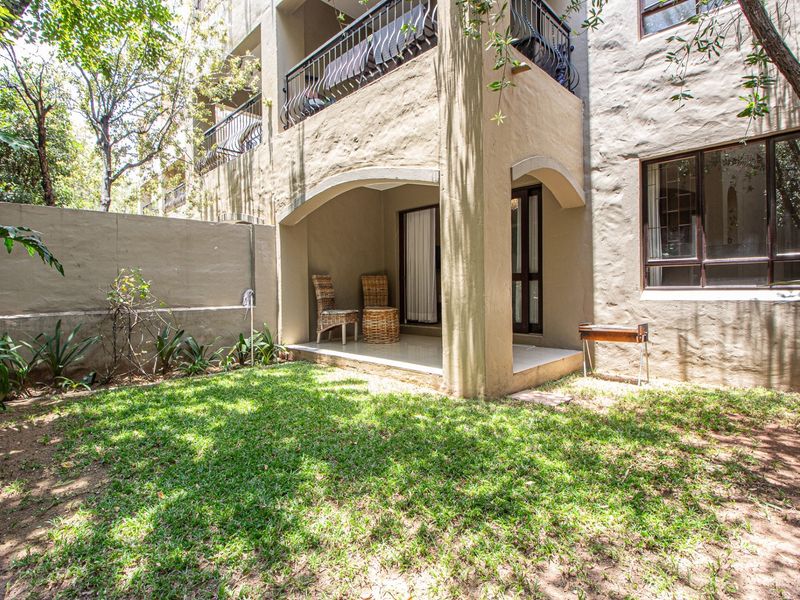 Ground floor apartment featuring a private covered patio and a small garden area with established trees and boundary walling.
