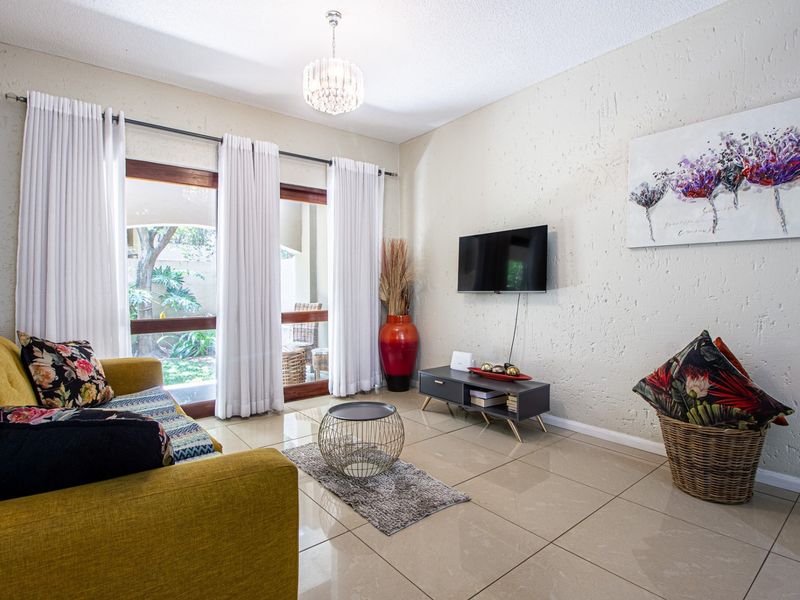 A bright living room featuring large sliding glass doors that open to a patio, complemented by neutral tiled flooring and textured walls.