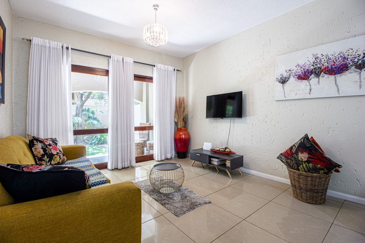 A bright living room featuring large sliding glass doors that open to a patio, complemented by neutral tiled flooring and textured walls.