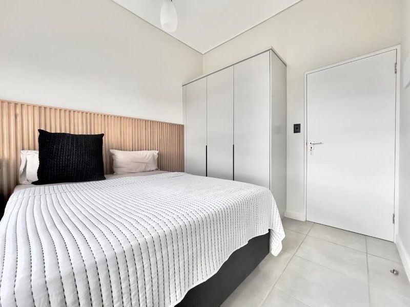 Modern bedroom featuring a timber slat feature wall, built-in wardrobe, and neutral tiled flooring.