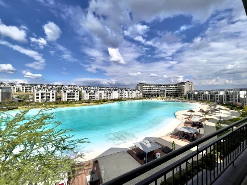 A scenic elevated view overlooking a large turquoise man-made lagoon with a sandy beach and surrounding residential apartment complex.