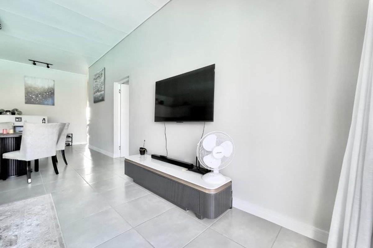A bright, open-plan living area featuring neutral tiled flooring and a clean, modern aesthetic with a recessed ceiling design.
