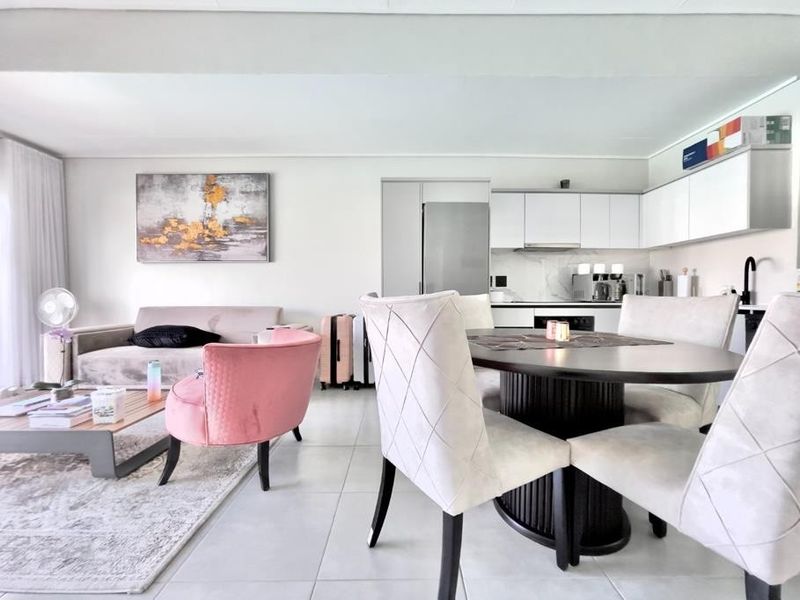 Modern open-plan living area featuring a contemporary kitchen with sleek white cabinetry, integrated appliances, and neutral tiled flooring throughout the combined space.