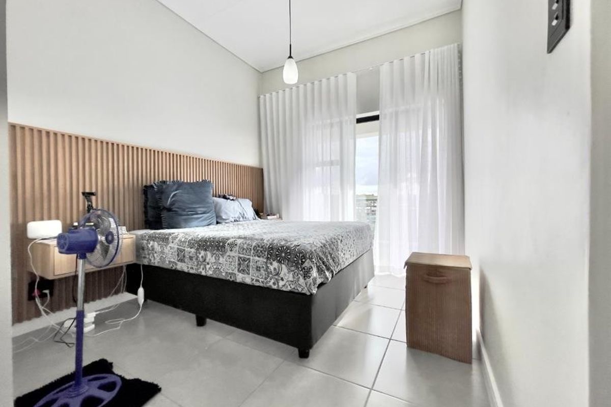 Modern bedroom featuring a decorative slatted timber headboard wall, tiled flooring, and direct access to a balcony through sliding glass doors.