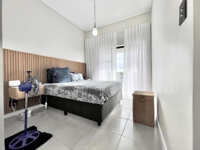 Modern bedroom featuring a decorative slatted timber headboard wall, tiled flooring, and direct access to a balcony through sliding glass doors.