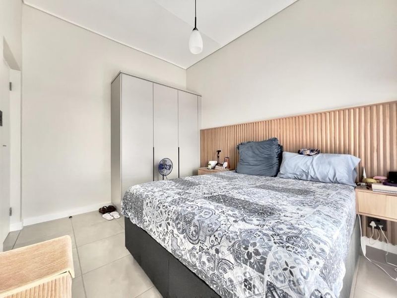 A modern bedroom featuring a slatted timber headboard wall, built-in wardrobe, tiled flooring, and contemporary pendant lighting.