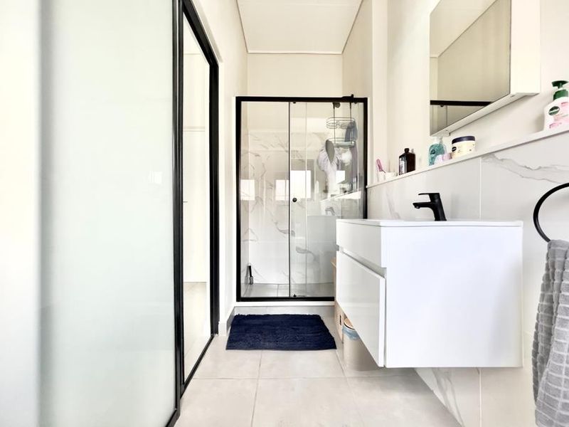 Modern bathroom featuring a floating vanity with a black faucet, a glass-enclosed shower, and contemporary marble-look wall tiling.
